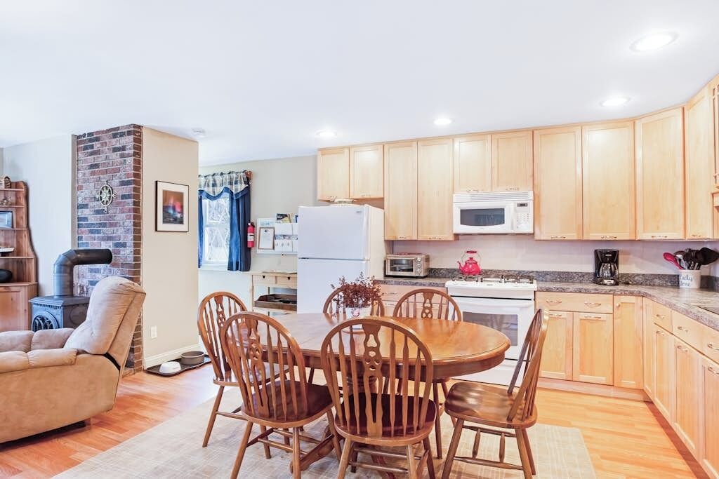 A kitchen with wooden cabinets, a microwave, a refrigerator, and a dining area with a table and chairs.