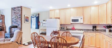 A kitchen with wooden cabinets, a microwave, a refrigerator, and a dining area with a table and chairs.
