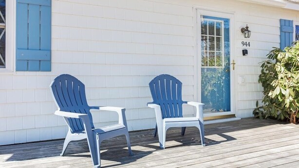 A house with a white exterior and blue shutters, a door with the number 944, and two blue Adirondack chairs on a wooden deck. - Dog-friendly Home in Great Locale Close to the Ocean With Yard, Streaming, W/D (Seal Cove)