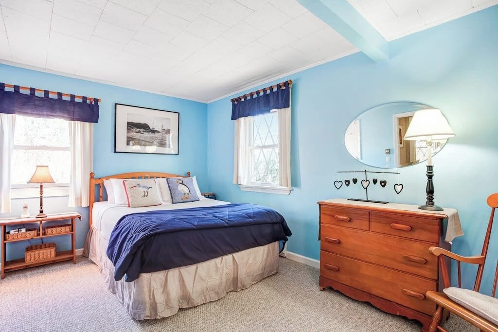 A bedroom with a bed, dresser, chair, and a window with curtains.