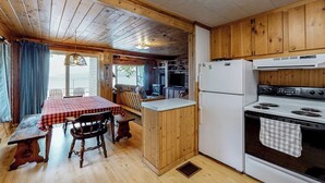 Uma cozinha estilo cabana com armários de madeira, uma mesa de jantar com cadeiras, um refrigerador e um fogão.
