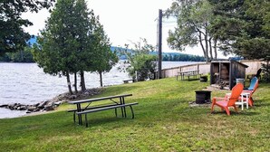 En picknickplats vid sjön med en bänk, stolar och ett litet förråd.