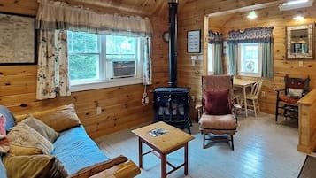 A wooden cabin interior with a sofa, a table, a chair, a fireplace, and a dining area.