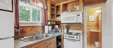 A compact kitchen with wooden cabinets, a microwave, a stove, and a sink.