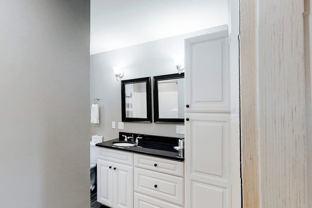 A bathroom with a double sink, white cabinetry, and two wall-mounted mirrors.