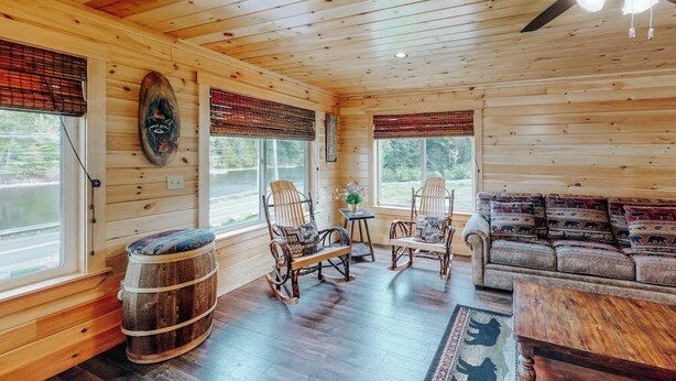 A wooden cabin interior with a sofa, rocking chairs, a table, and a barrel. - Charming Riverfront Home With Mountain Views & Private Dock (Rockwood)