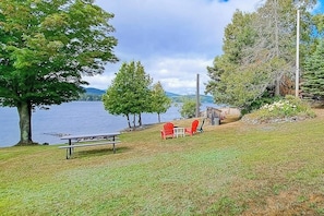 Vista a un lago con una mesa y sillas de picnic, rodeado de árboles y una estructura de madera.