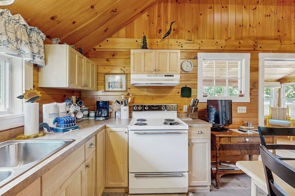 L’intérieur d’un chalet en bois comprend une cuisine équipée d’un poêle, de placards et d’un coin repas avec une table et des chaises.