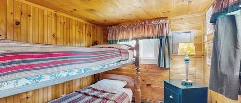 Une chambre de style cabane avec deux lits superposés, un plafond en bois, une petite table de chevet avec une lampe et une fenêtre avec des rideaux.