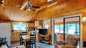 A wooden cabin interior with a dining area, kitchen, and a TV. - Lakefront, Cabin-inspired Home With Firepit, Grill, & Screened Porch, Wifi (Greenville)
