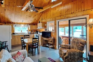 Interior de una cabaña de madera con comedor, cocina y televisor.