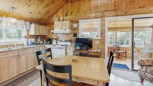 A wooden interior with a kitchen, dining area, and large windows. - Lakefront, Cabin-inspired Home With Firepit, Grill, & Screened Porch, Wifi (Greenville)