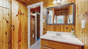 A wooden-paneled bathroom with a white sink, a mirror, and a door leading to another room.