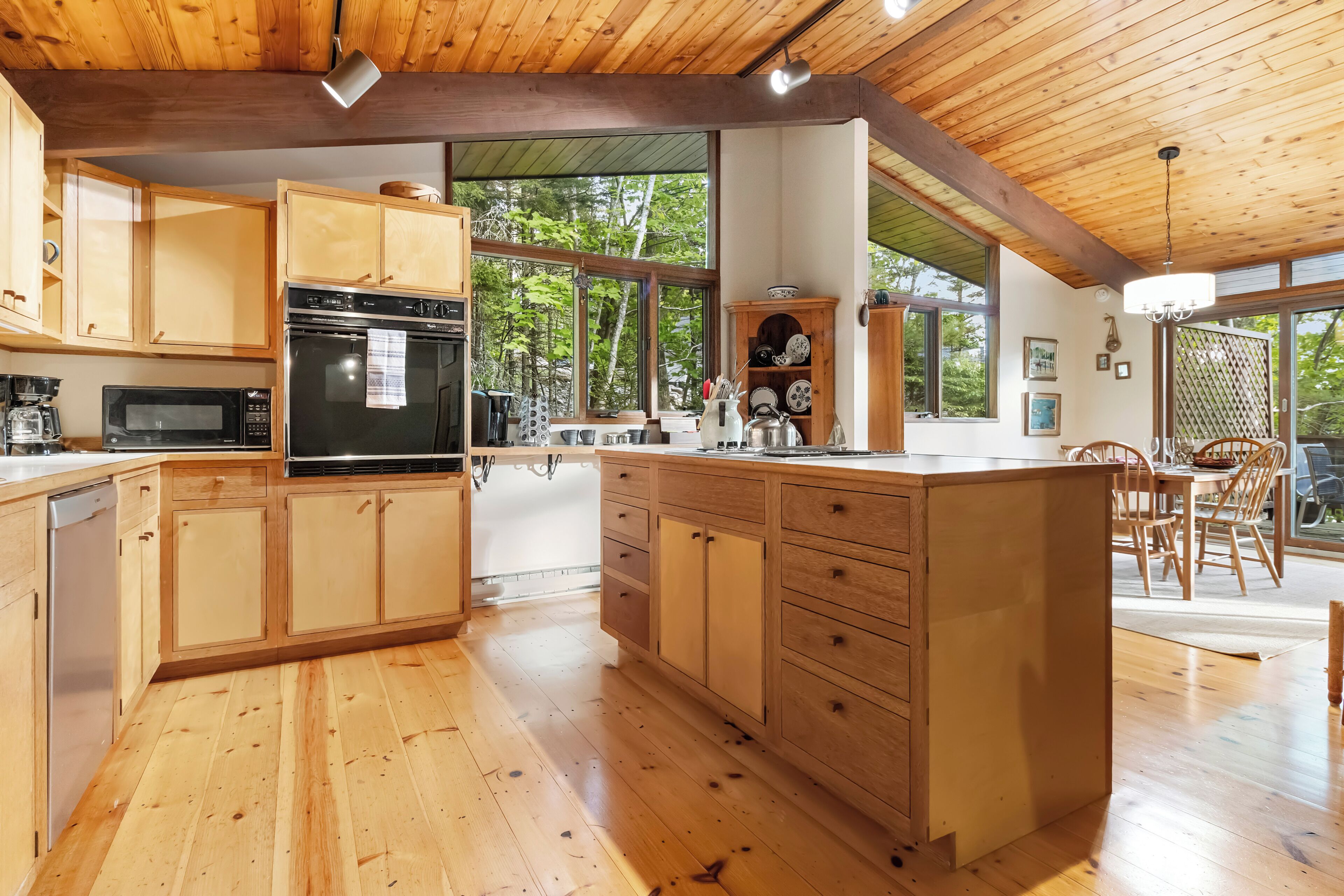A wooden kitchen with a large island, built-in appliances, and a view of the outdoors.