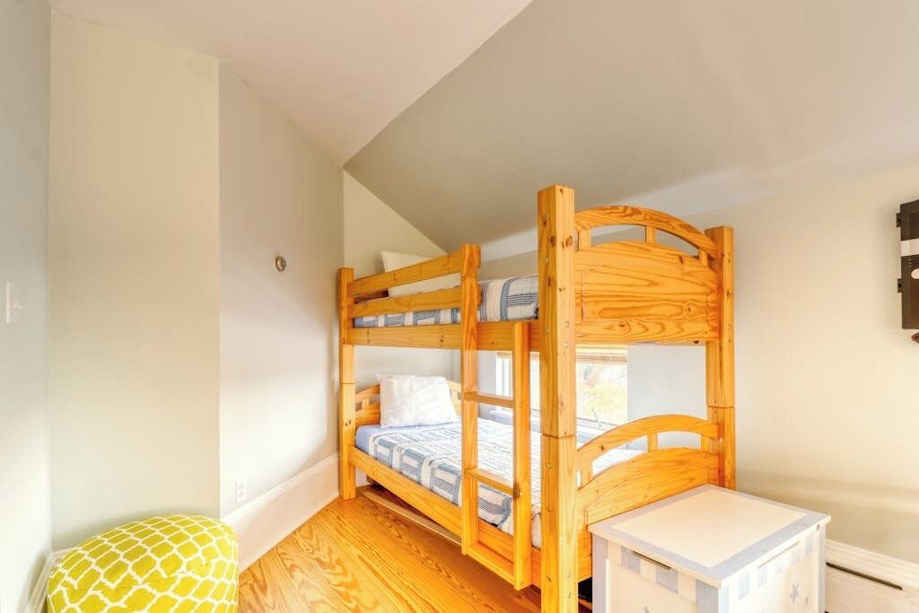 Un lit superposé avec une structure en bois, une petite table de chevet et un coussin jaune à motifs.