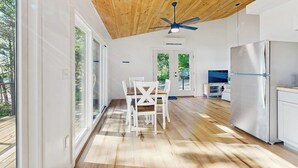 A modern kitchen with a wooden ceiling, large windows, and a dining area with white furniture. - Modern Maine Cottage With River Views, Deck, and a Convenient Washer/dryer (Stockton Springs)