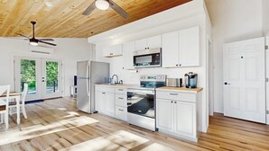 A modern kitchen with white cabinets, stainless steel appliances, and a wooden ceiling. - Modern Maine Cottage With River Views, Deck, and a Convenient Washer/dryer (Stockton Springs)