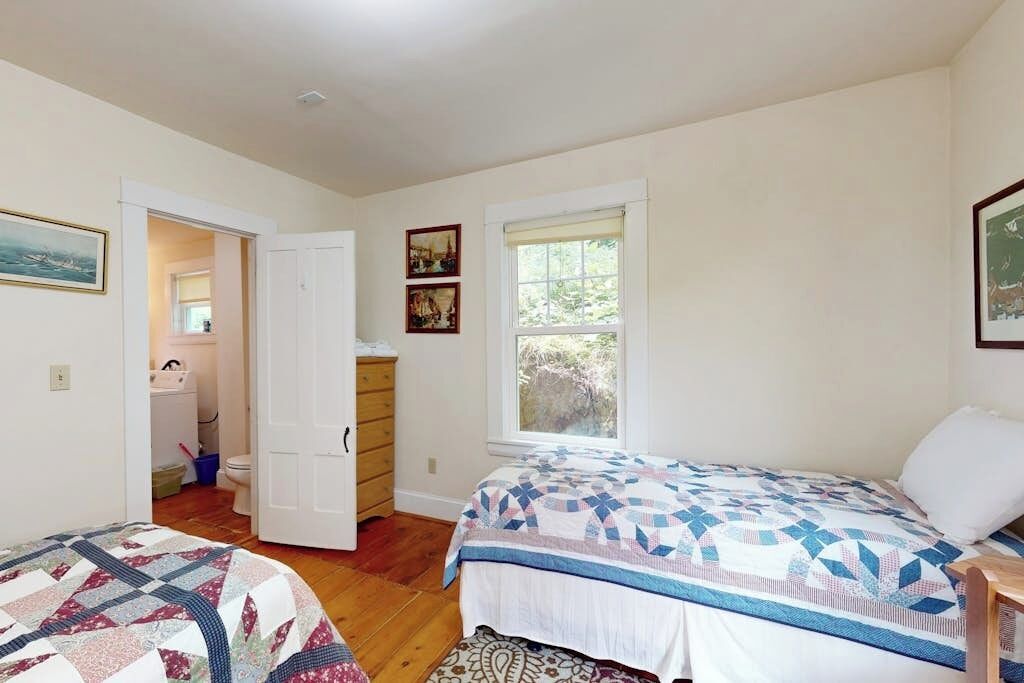 Een slaapkamer met een bed, een dressoir, een raam en een deur die leidt naar een badkamer.