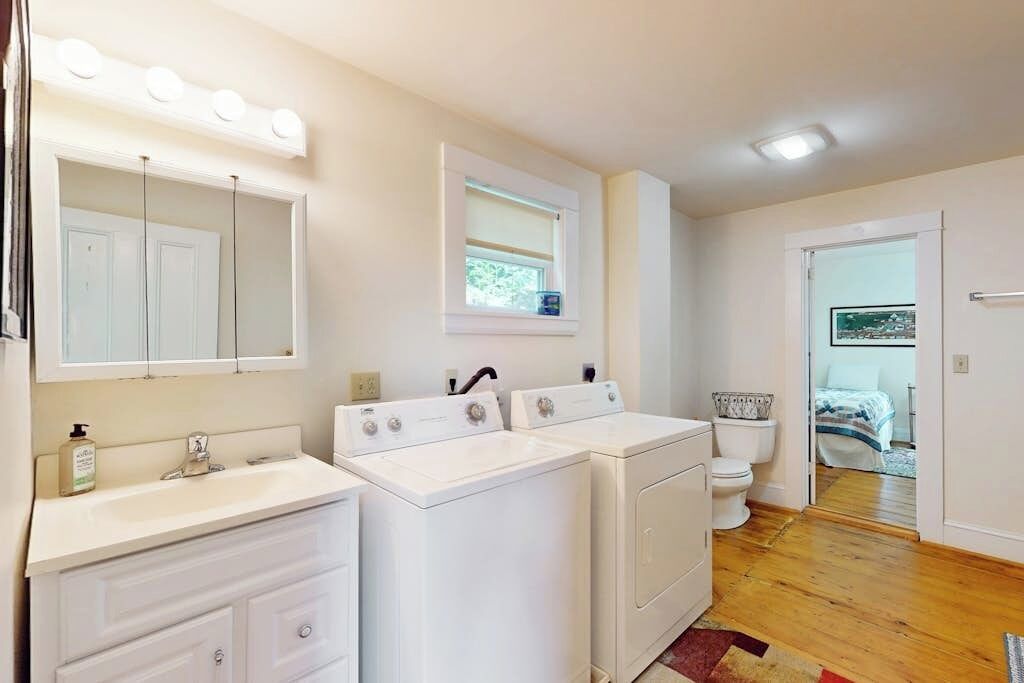 A laundry room with two washing machines, a sink, and a mirror with lights.