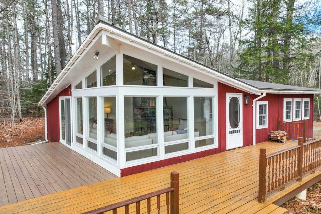 A two-story cabin with large windows, a wooden deck, and a red exterior.