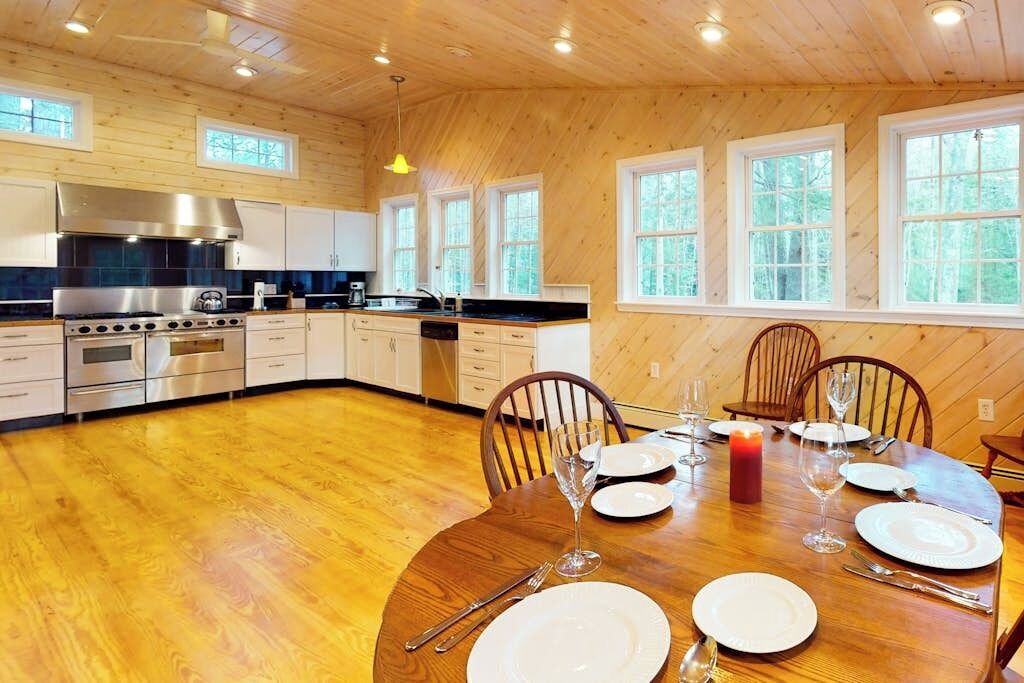 A wooden-paneled kitchen with a central island, white cabinetry, and a dining area set for six with a candle.