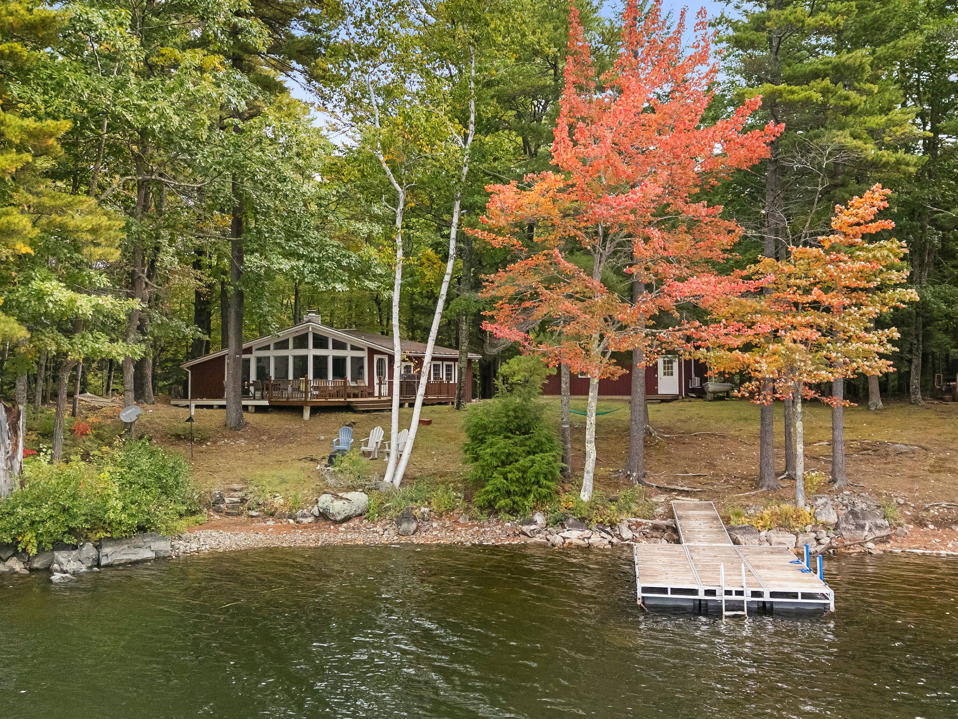 A cabin with a dock extending into a lake, surrounded by trees and a grassy area.