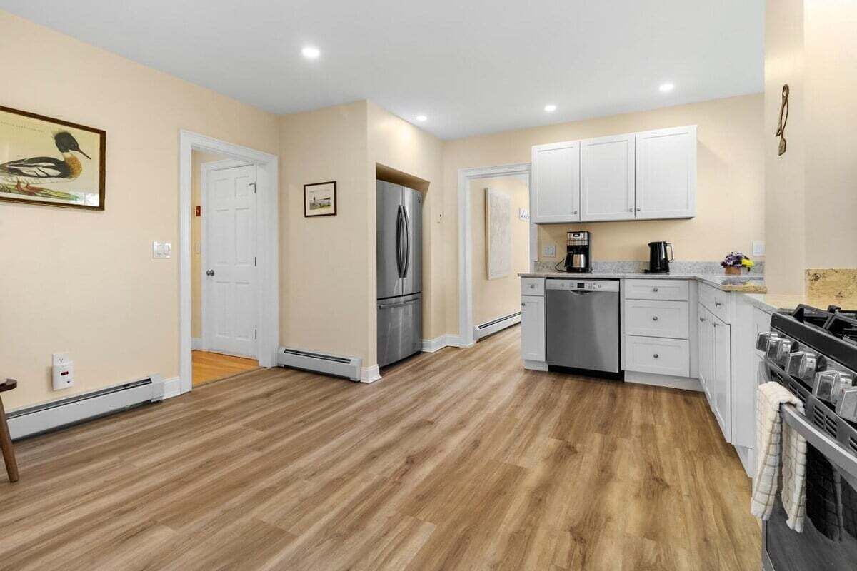 Una cucina moderna con mobili bianchi, frigorifero in acciaio inossidabile, lavastoviglie e piano cottura a gas.