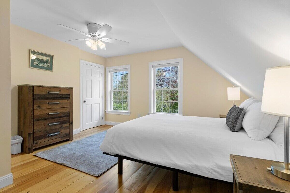 A bedroom with a bed, a dresser, a ceiling fan, and windows.