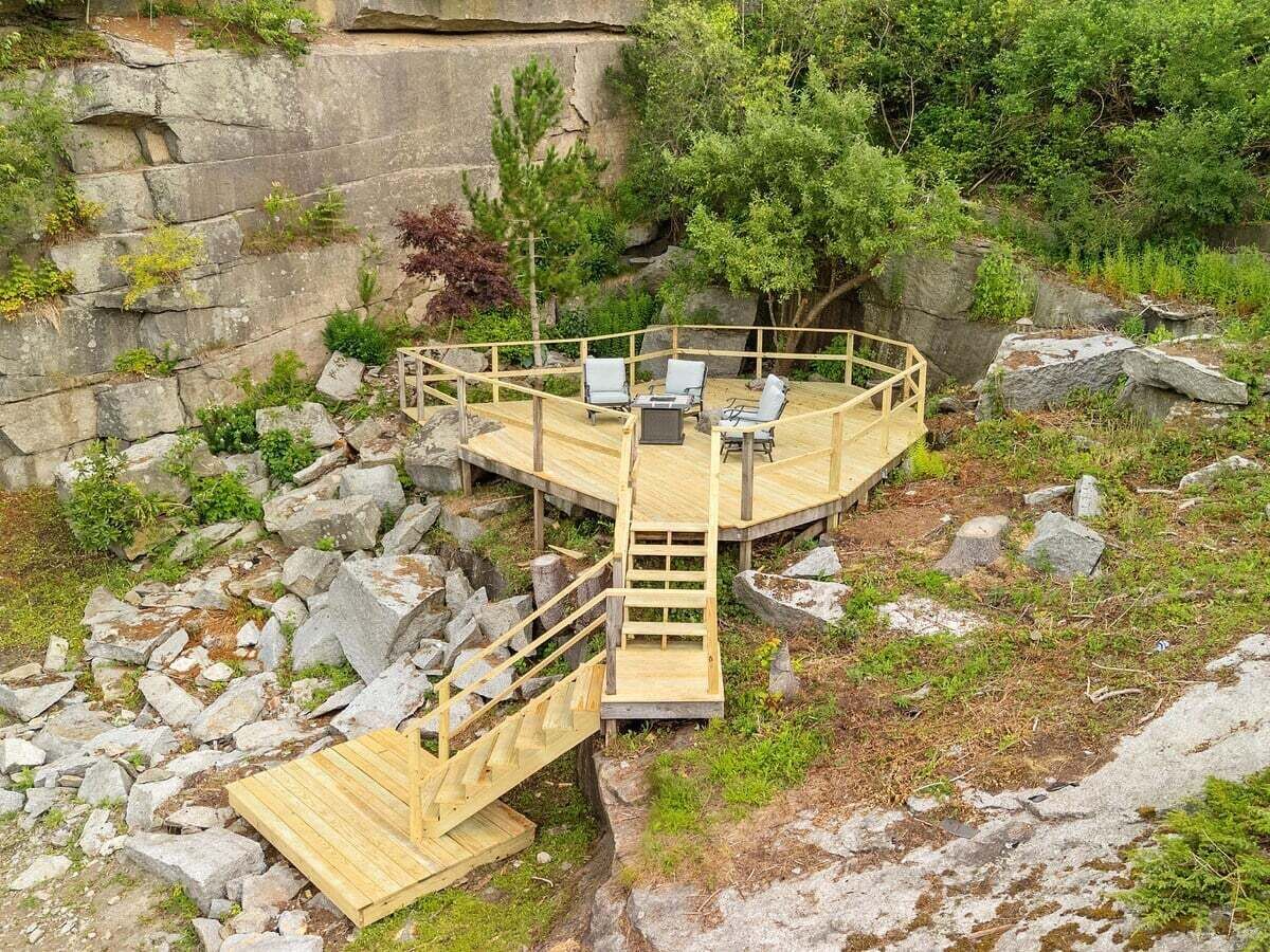 Une terrasse en bois avec un escalier menant à un espace de détente circulaire, comprenant des chaises et une table.