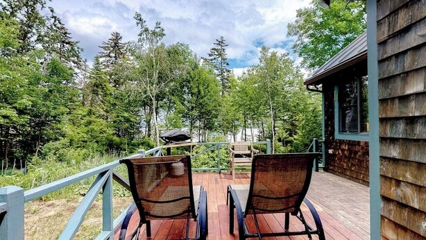 A wooden deck with two chairs, a barbecue grill, and a view of a forested area. - Dog-friendly Lakefront Home w/ Deck, Firepit, Water Views & Games (Rockwood)