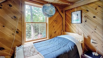 Une chambre dans une cabane en bois, avec un lit, une fenêtre, un globe terrestre et un tableau encadré.