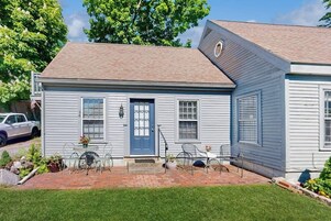 A single-story house with a blue front door, a small porch with chairs, and a brick pathway leading to the entrance.