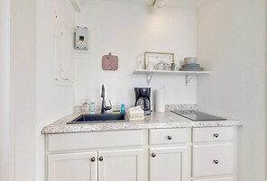 A kitchen with a sink, countertop, cabinets, a coffee maker, and a shelf with dishes.