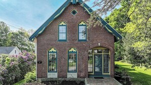 A two-story brick house with a gabled roof, a front porch, and a small front yard. - Elegant Victorian Gothic Revival Home With wet Bar, Sunroom, & Washer/dryer (Belfast)