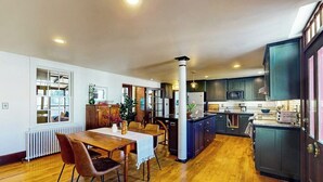 A spacious kitchen with dark cabinets, a central island, and a dining area with a wooden table and chairs. - Elegant Victorian Gothic Revival Home With wet Bar, Sunroom, & Washer/dryer (Belfast)