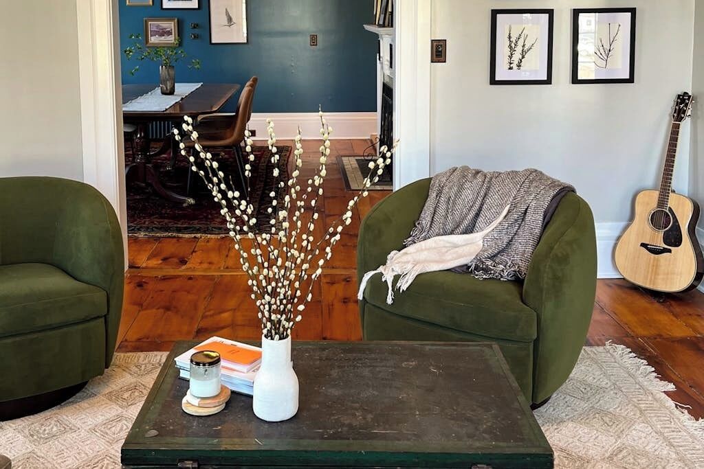 Un salon avec deux fauteuils verts, une table basse, un vase orné de branches et une guitare.