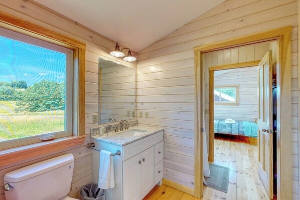 A wooden cabin bathroom with a toilet, sink, and mirror. - Bayfront Home With Gorgeous Water Views, Dock, Outdoor Patio, Fireplace (Bowdoinham)
