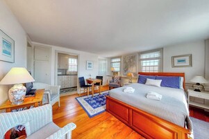 A hotel room with a wooden bed, a desk, a chair, a small table, and a sofa.