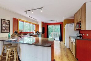 A modern kitchen with a central island, wooden cabinets, and a large window. - Summertime (Bar Harbor)