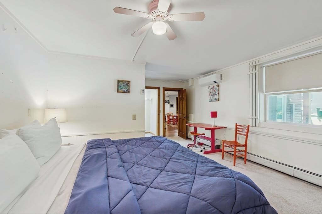A bedroom with a bed, a desk, a chair, and a ceiling fan.