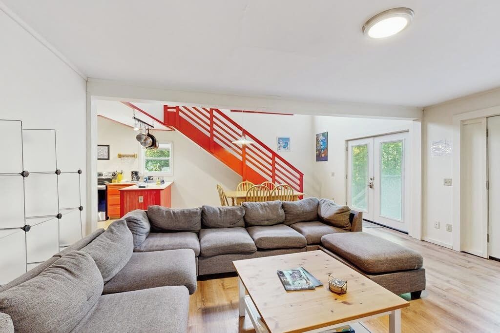 A modern living room with a sectional sofa, a wooden coffee table, and a red staircase.