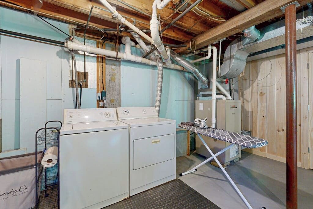 A laundry room with two washing machines, an ironing board, and visible plumbing.
