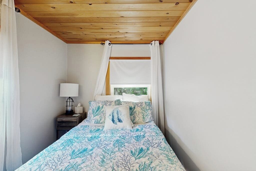 A bedroom with a bed, a nightstand, a lamp, and a window with curtains.