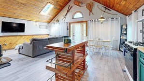 A loft-style room with a wooden ceiling, a sofa, a dining table, and a kitchen area. - Scenic Retreat With a Spacious Deck, gas Fireplace, and Moosehead Lake Views (Greenville)