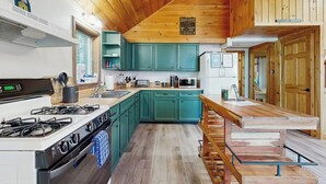 A kitchen with teal cabinets, a wooden ceiling, a gas stove, and a wooden bench. - Scenic Retreat With a Spacious Deck, gas Fireplace, and Moosehead Lake Views (Greenville)
