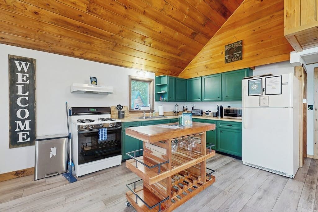 Eine Küche mit Holzbalkendecke, grünen Schränken, einem weißen Kühlschrank und einem Weinkühler.