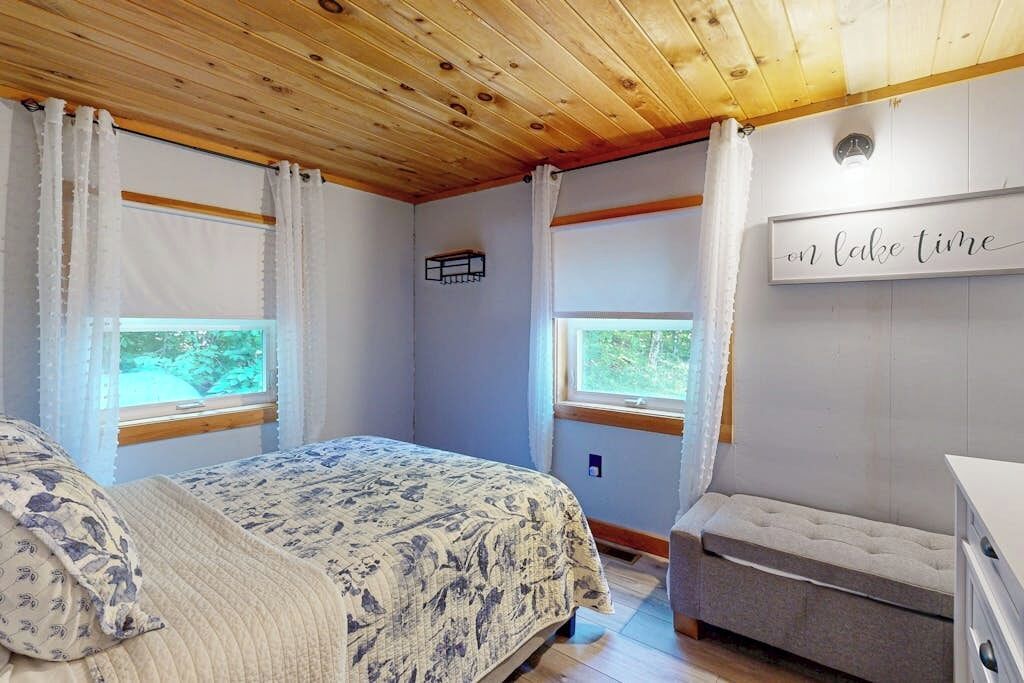 A bedroom with a bed, a bench, a window, and a wall-mounted sign.
