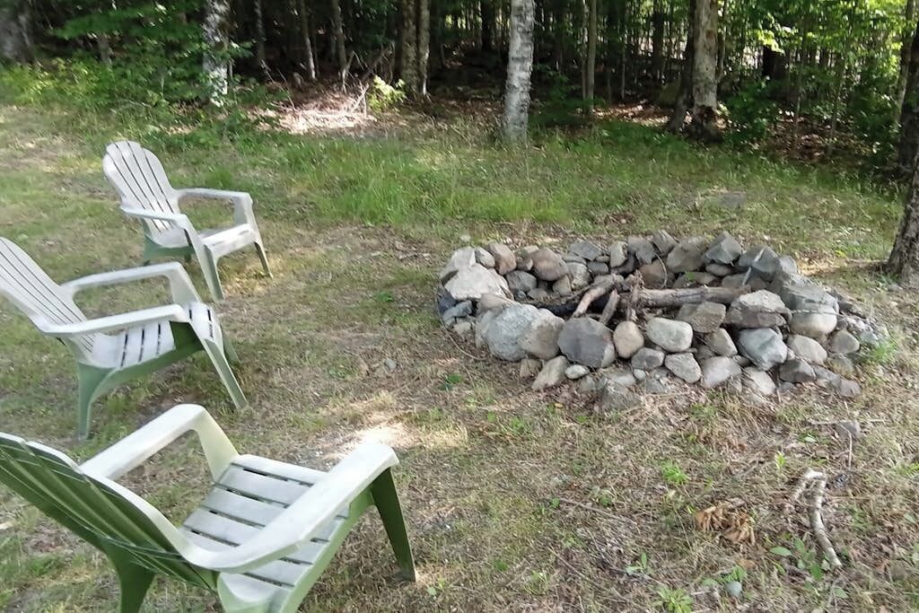 Leirintäalue, jossa on nuotiopaikka ja sen ympärillä vihreitä Adirondack-tyylisiä tuoleja.