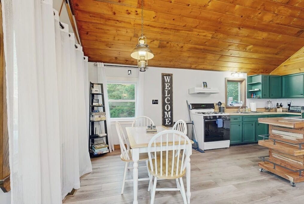 A kitchen with wooden cabinets, a stove, and a dining area with chairs.