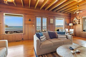 Ein Holzinterieur mit einer Couch, einem runden Couchtisch und Blick aufs Meer.